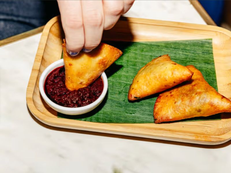 Crisp sambusas with a beet-red dipping sauce on a banana leaf