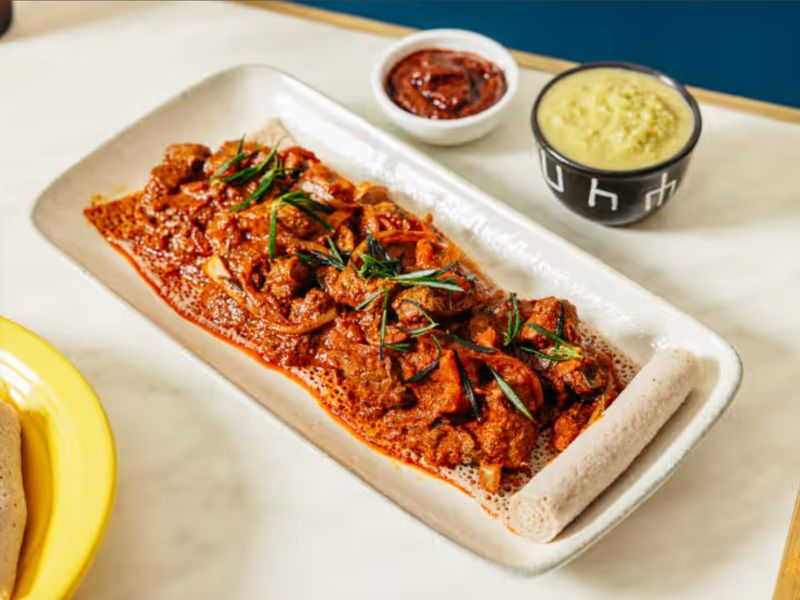 Zigni stew over injera with two dipping sauces